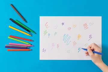 The child learns to draw on a white sheet of paper on a blue background.