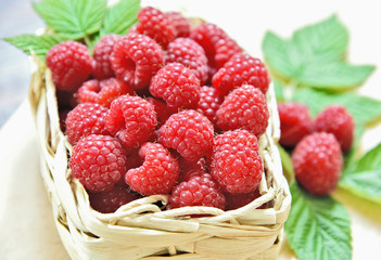 A lot of fresh Raspberry with green leaf in basket on wooden table.