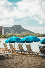 Sun lounges and beach umbrellas set up on Waikiki Beach, Hawaii with Diamond Head Crater visible in...