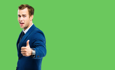Excited businessman showing thumbs up like hand sign gesture, in blue confident suit, over green...