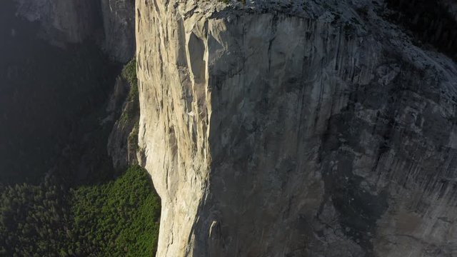 Vertical granite slopes of Mount El Capitan are in frame. Huge monolith, popular among rock climbers. one of the slopes is lit by the setting sun. Yosemite National Park. Aerial, 4K