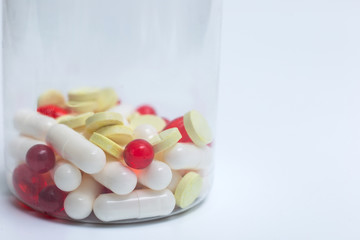 Multi-colored assorted tablets and capsules lie in a transparent bottle.