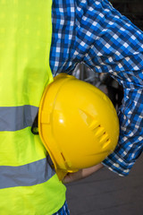 Cropped image of a construction worker wearing a yellow safety vest and keeping a yellow helmet underarm