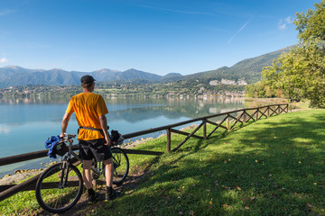 Stunning italian lake. Lake Pusiano with in the background the town of Pusiano view from Bosisio Parini lake front. Tourist man with bicycle on lake observes the panorama