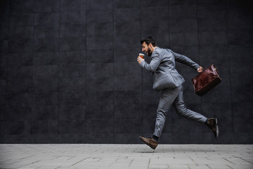 Young fashionable businessman running on the street. He is late for work.