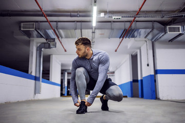 Young man crouching and tying shoelace in underground garage.