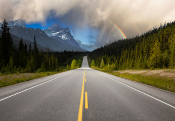 Scenic road in the Canadian Rockies during a vibrant sunny summer day with Rainbow. Rainy Sky Composite. Taken in Icefields Parkway, Banff National Park, Alberta, Canada.