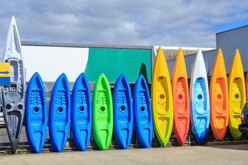 A row of colorful plastic kayaks of various sizes, leaning against a fence
