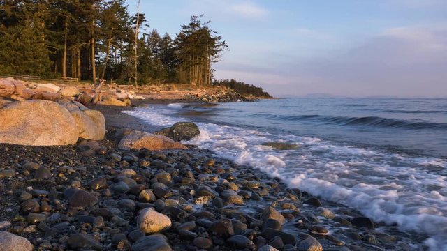 Rocky beach with saves and pan up to beautiful coast line in golden sunrise light.