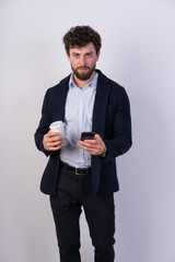Confident business man drinking coffee and phone in hand, he looks directly into the camera