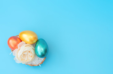 Decorated Easter eggs lie in the basket like a nest with white flower on blue background. Happy Easter holiday concept. Greeting or invitation card. Flat lay style with copy space.