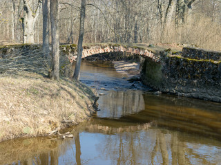 Fototapeta na wymiar The Masonry bridge bridge over the river of Cuja, a sunny day in early spring with clear blue skies, the banks of a small river