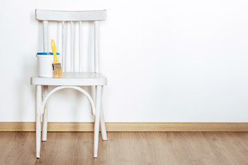 Upcycling concept. Repainting an old chair. Old white wooden chair on beige floor against white wall