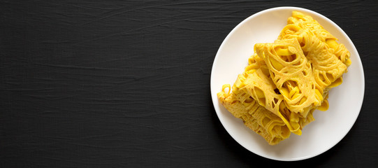 Homemade Net Crepe Roti Jala on a white plate on a black background, top view. Flat lay, overhead, from above. Space for text.