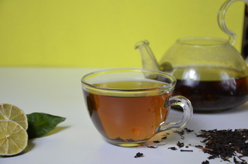 Transparent cup and teapot with black tea, dry tea brewing on the table, bergamot slices, or lemon...