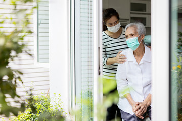 Verzorgervrouw zorgt voor ouderen, depressieve senior wacht op haar familie om thuis te bezoeken, sociale afstand, nostalgie, stress, levensdepressie, thuisblijven tijdens Covid-19, Coronavirus pandemie