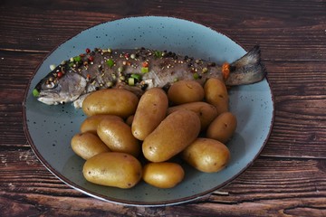 baked trout with pepper and boiled potatoes in a white plate on a wooden table