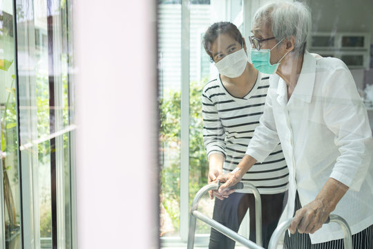 Asian daughter take care of senior mother,elderly woman is looking outside through window feeling bored,depressed,stressed,life depression of old people,stay home during Covid-19,Coronavirus pandemic