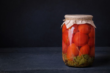 Fermented preserved vegetarian food concept. Pickled or salted canned tomatoes on dark background with copy space