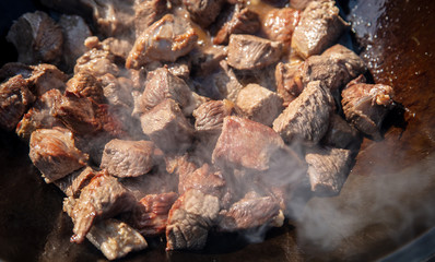 The meat is fried in oil on a cast-iron cauldron.