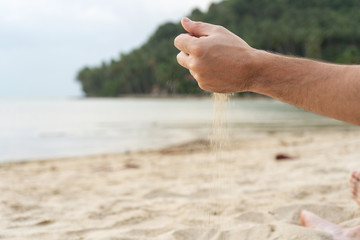 Play with sand on the beach. Sand is poured from the hands, against the backdrop of a tropical island.