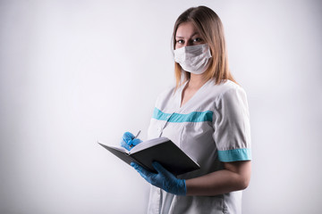 young woman in white clothes holding a gray diary. Female doctor, medical professional is writing down a prescription. masked doctor