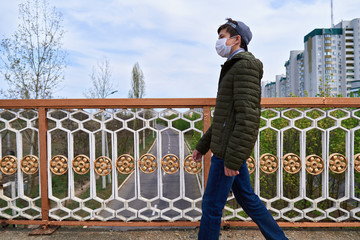 teen boy walks down the street during the day, a pedestrian walkway and high-rise buildings with apartments, a residential area, a medical mask on his face protects against viruses and dust