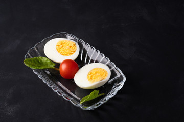 halves of boiled egg, tomato, greens on a dark background

T