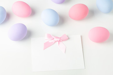Blank white greeting card with pink ribbon bow and pastel easter eggs on white table background, Easter background