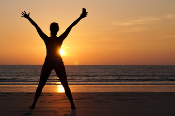 Fototapeta premium A young happy woman celebrating the end of lock down, on the beach at sunset after the coronavirus pandemic