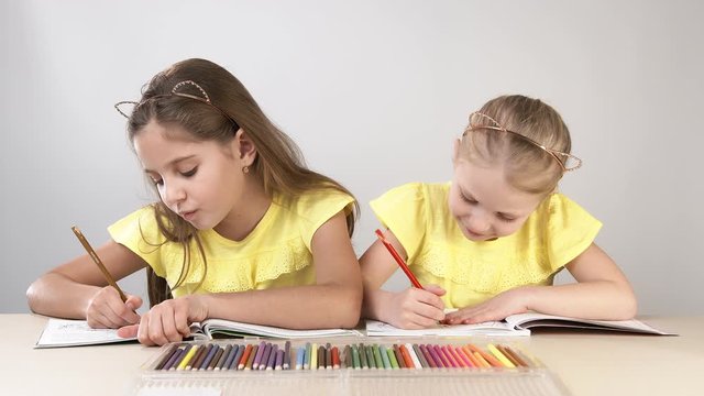 Funny and funny children. Children at the table dance and create. Two children are sitting at a table and coloring a coloring book.