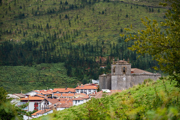 Fototapeta na wymiar Old traditional houses at the village with medieval church and green mountains. Typical rural village in the mountains of Basque Country, Spain. Camino de Santiago.