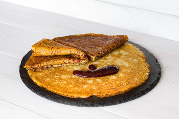 Sweet crepes, thin pancakes with fruit jam on a black stone plate. Wooden background. Side view