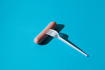 Raw sausage on a blue background with a plastic fork