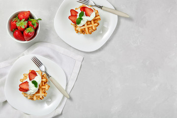Beautiful breakfast. Belgian Viennese waffles decorated with cream and strawberries,  tea and a napkin on a light background, top view.