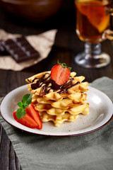 Beautiful breakfast. Belgian Viennese waffles decorated  with chocolate and strawberries, tea on a dark background.