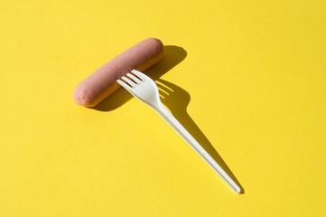 Sausage and white plastic fork on a bright yellow background with hard light