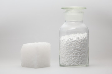 glass laboratory jar with samples of white synthetic rubber and a cube of white rubber next to it...