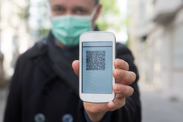 portrait of man with a medical mask showing a qr code on the screen of his smartphone for a police check on the street during the covid-19 pandemic