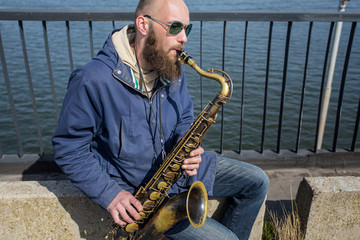 Fototapeta premium a handsome male saxophonist with glasses plays on the streets of the city