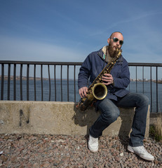 a handsome male saxophonist with glasses plays on the streets of the city