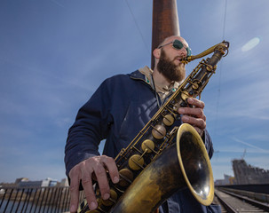 a handsome male saxophonist with glasses plays on the streets of the city