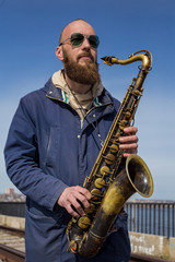 a handsome male saxophonist with glasses plays on the streets of the city