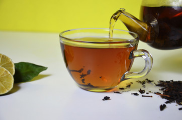 Pouring Healthy Tea over white Transparent cup and teapot with black tea, dry tea brewing on the...
