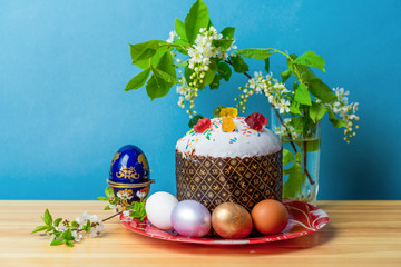 bird cherry branch next to easter cake and colorful easter eggs on wooden table