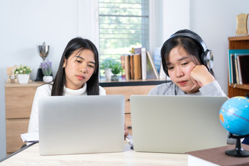 Happy Asian woman students learning e-learning wearing headphones for talking watching video conference online by laptop computer, sitting study prepare project homework with happiness time in room