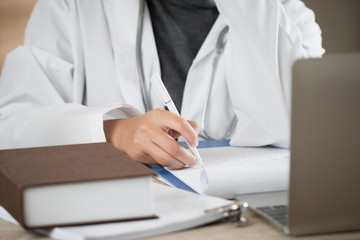 Medicine doctor hand writing prescription clipboard record information of patient in clinic, Female physician working on laptop computer and stethoscope in hospital. Healthcare and medical concept