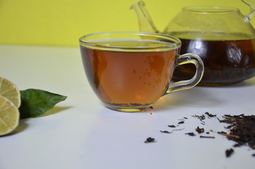 Transparent cup and teapot with black tea, dry tea brewing on the table, bergamot slices, or lemon or lime on a white background with cinnamon and anise