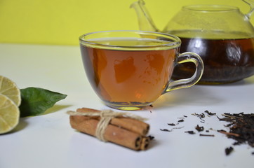 Transparent cup and teapot with black tea, dry tea brewing on the table, bergamot slices, or lemon or lime on a white background with cinnamon and anise