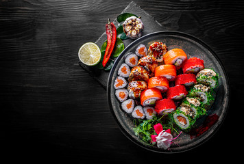 set of sushi roll with salmon, avocado, cream cheese, cucumber, rice, caviar, eel in plate on black wooden table background